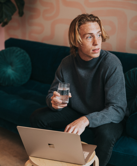 Man with laptop looking to the left while holding a glass of water